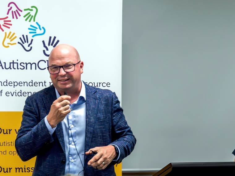 A man speaks into a microphone infront of an Autism CRC banner.