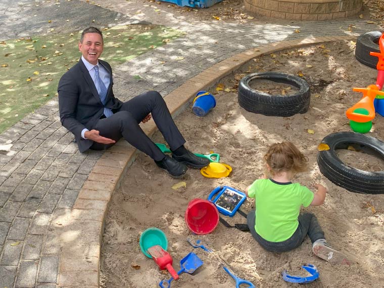A man in a suit happily plays in a sandpith with a child