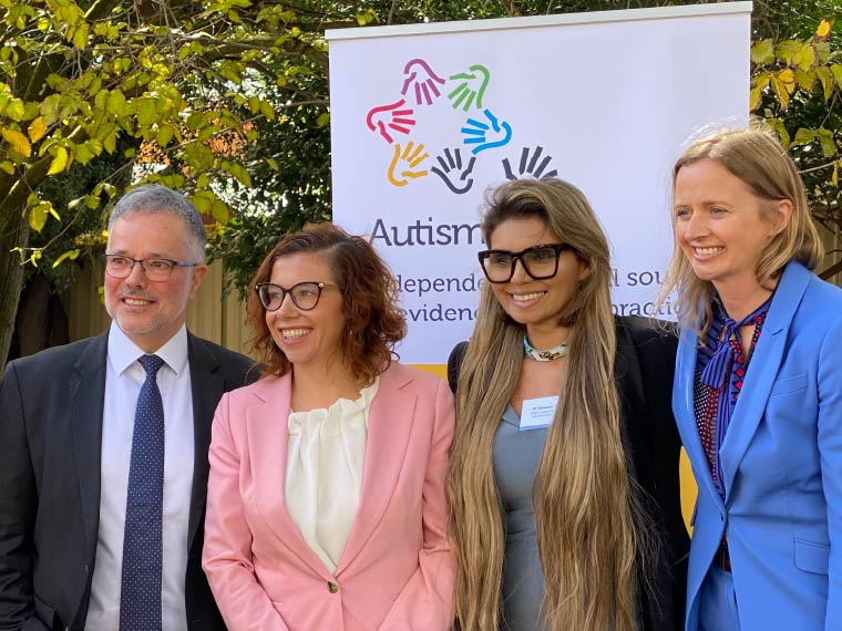 A group of four people stand posed, in front an Autism CRC banner