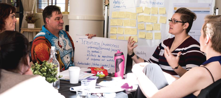 Five people sit at table together. One person is talking while the others are listening.