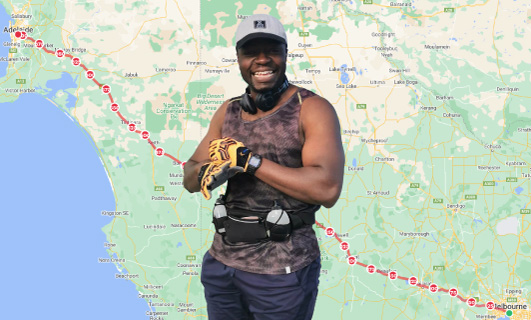 George Chijarira standing in front of a map showcasing his route from Adelaide to Melbourne