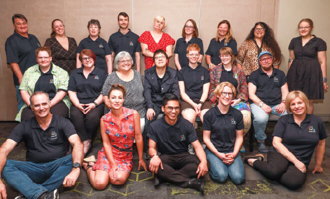 A large group of people stand or sit, many wearing a dark blue shirt with Autism CRC logo, looking towards the camera.