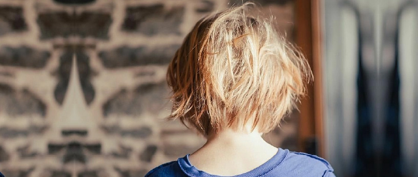 A young child with slightly messy hair facing away from the camera