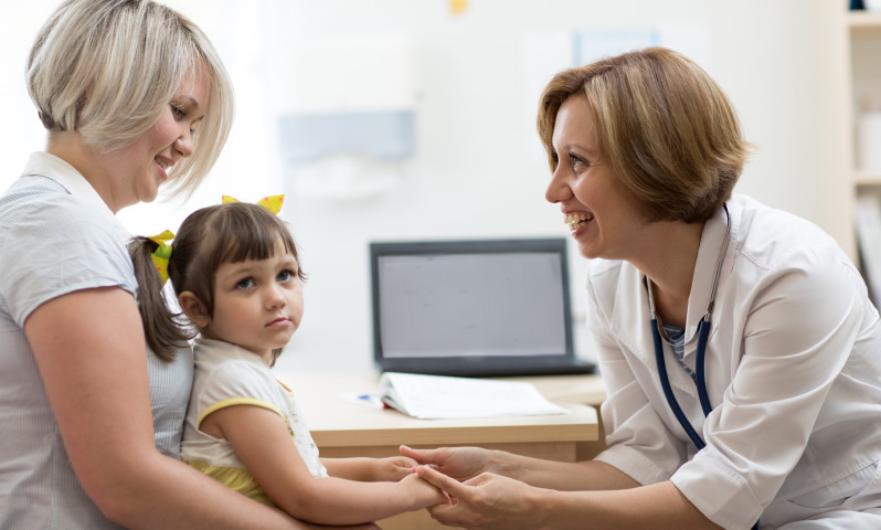 A doctor talking to a young child who is sitting in the lap of their parent