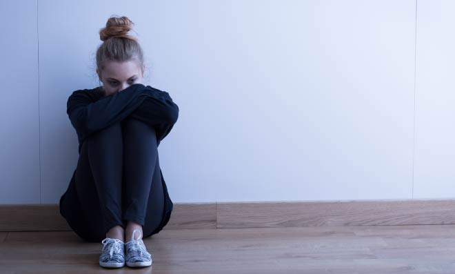 A young adult sits on the floor, holding themself