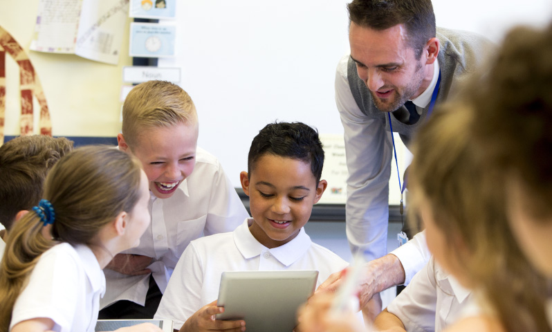 A teacher and a group of students looking at a tablet computer