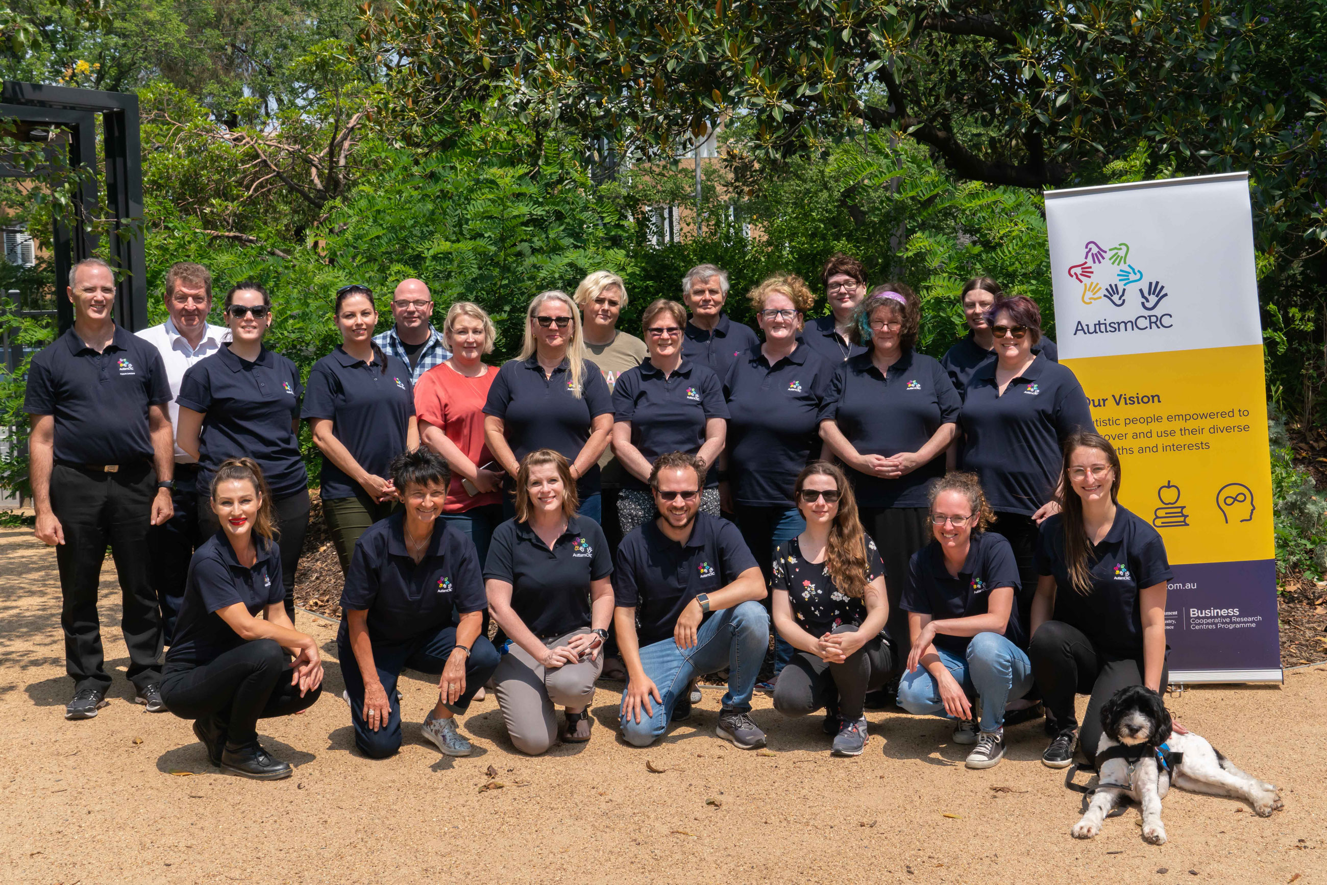 A large group of people stand or sit, many wearing a dark blue shirt with Autism CRC logo, looking towards the camera.