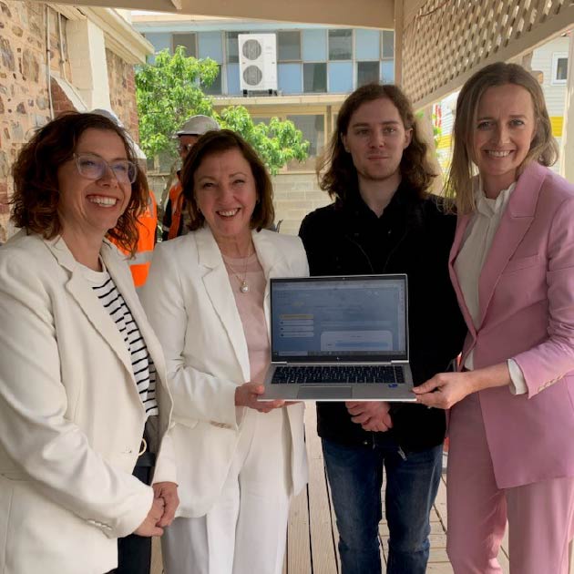 A group of smiling people hold a laptop, showing the website myWAY Employability