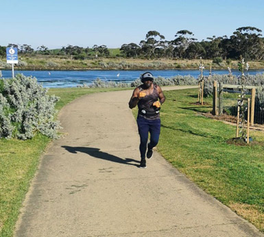 George Chijarira running on a path through a green field, with a lake in the background