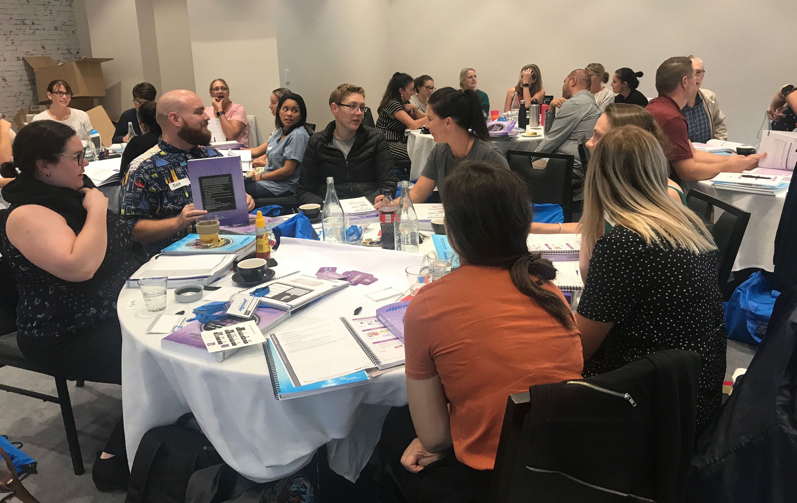 Teachers sit in groups around large circular tables with a variety of Secret Agent Society Resources in front of them