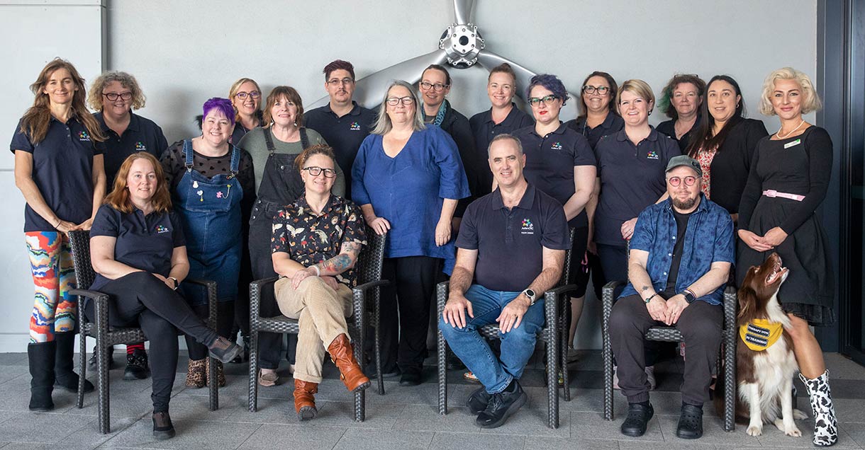 A large group of people stand or sit, many wearing a dark blue shirt with Autism CRC logo, looking towards the camera.