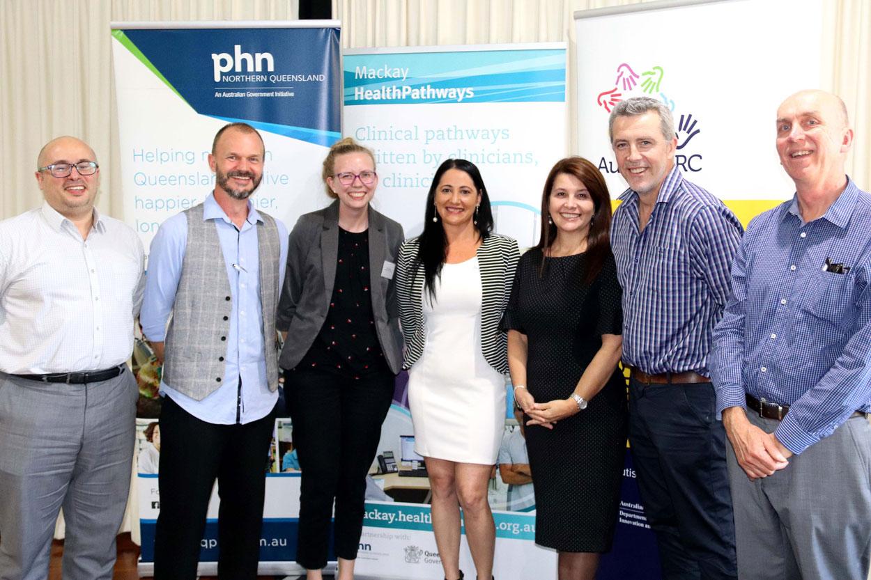 Seven people stand in in front of banners for phn Norther Queensland, Mackay HealthyPathways and AutismCRC